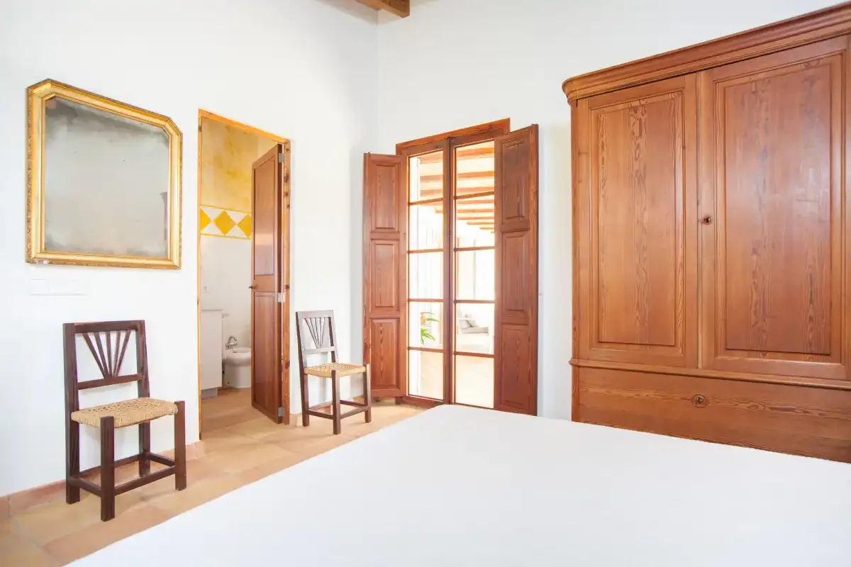A bedroom with a bed, wooden chairs, and a large wooden wardrobe.