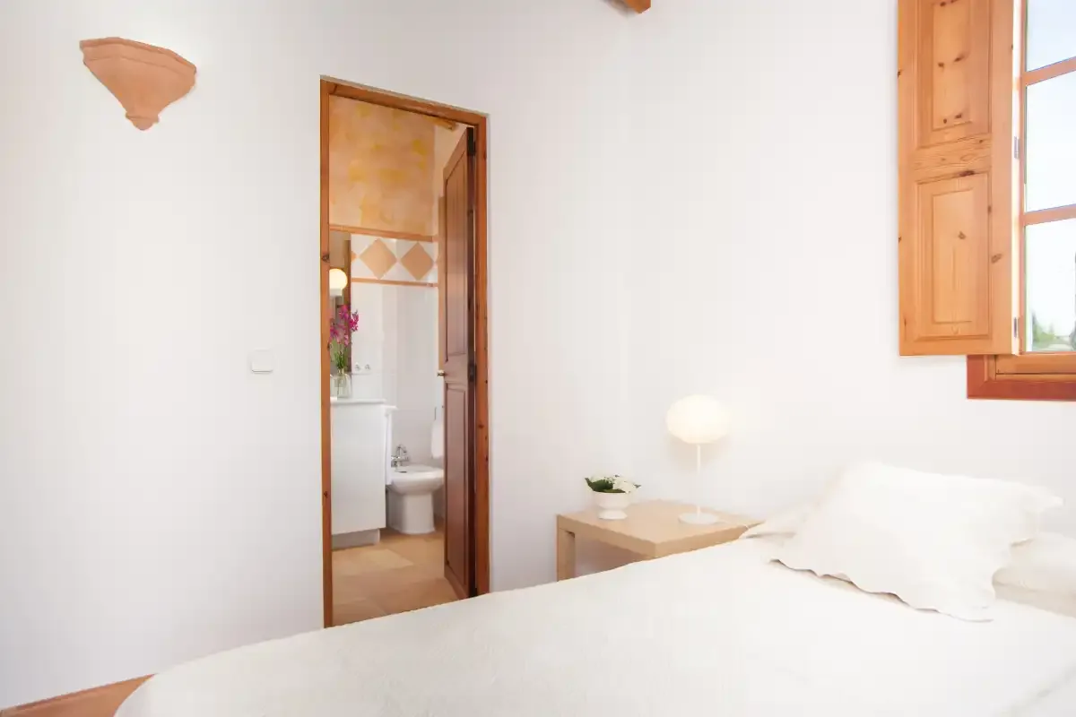 A bright bedroom with a bed beside an open wooden window.
