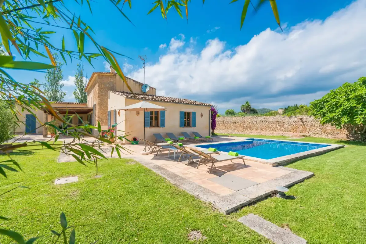 A house and swimming pool sit beside a lawn and stone wall.
