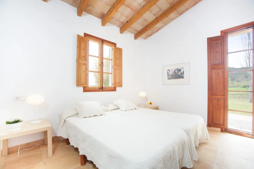 A bright bedroom has a double bed beneath a timber-beamed ceiling.
