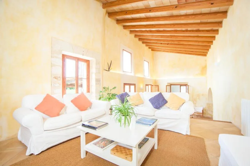 A bright living room with seating around a coffee table beneath exposed wooden beams.