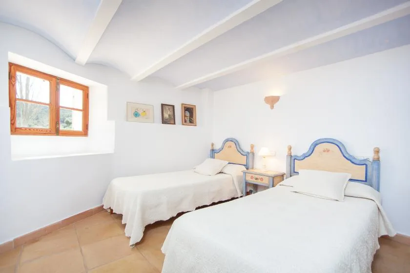 A bright bedroom with two beds and a wooden-framed window.