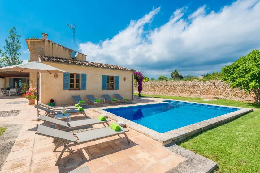 A swimming pool beside a house, with sun loungers arranged on the patio.
