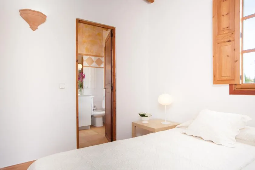 A bright bedroom with a bed beside an open doorway to a bathroom.