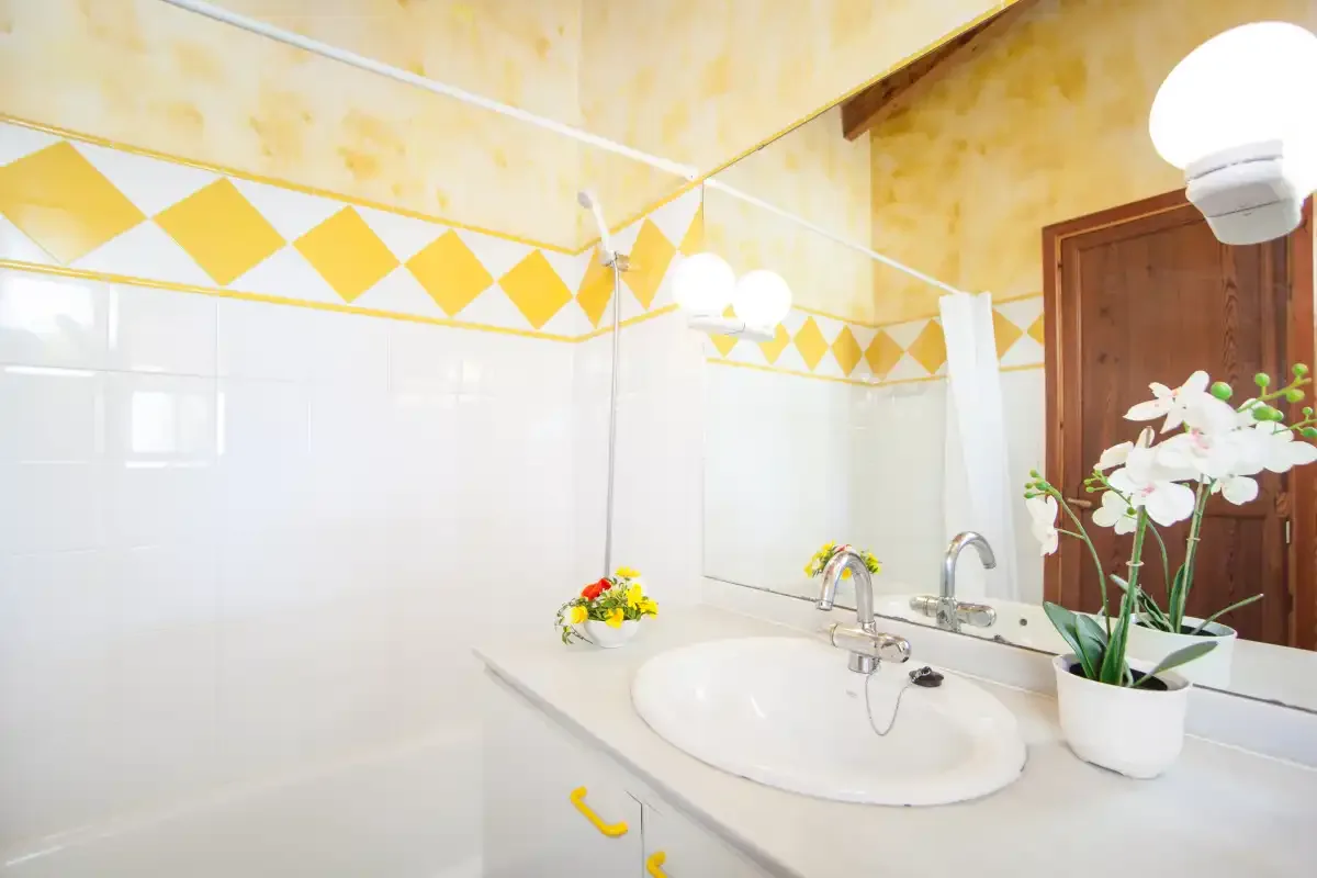 A bright bathroom with a sink, mirror, and yellow tile accents.