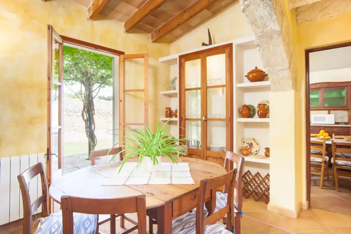 A dining area with a wooden table and chairs sits beside open windows.