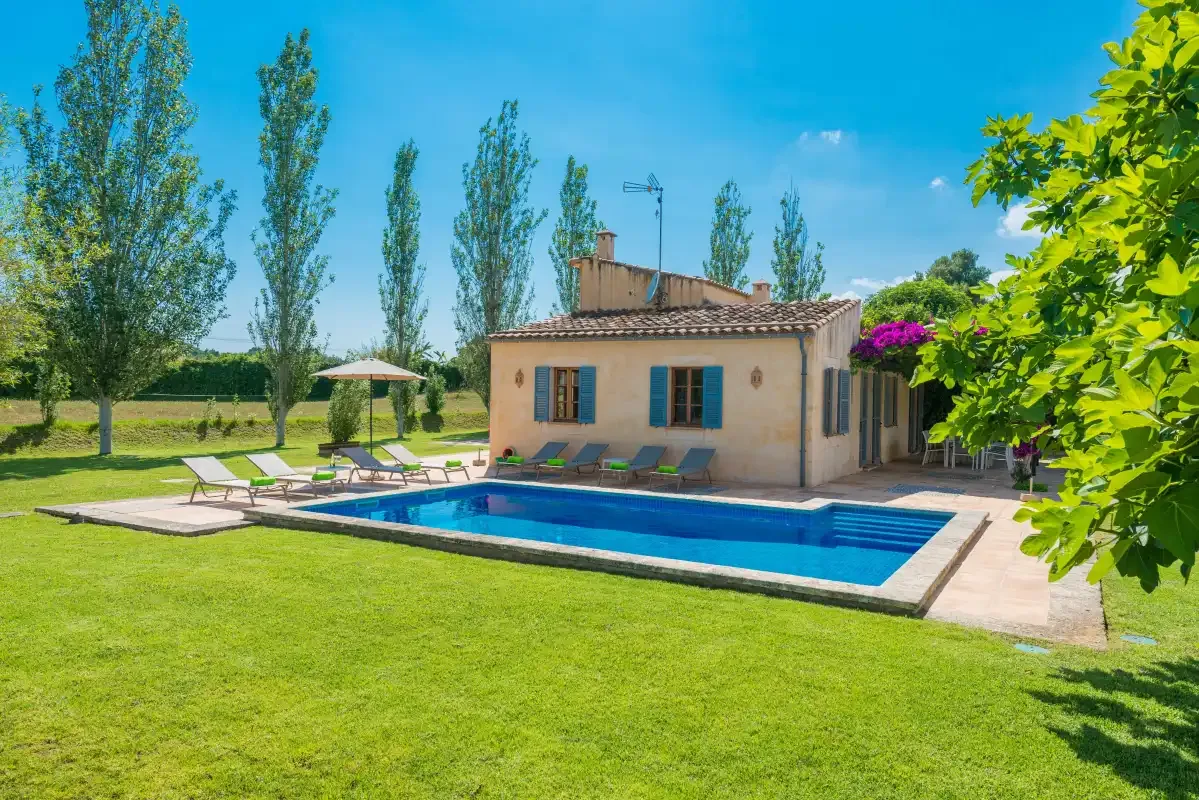 A small house stands beside a swimming pool on a broad green lawn.