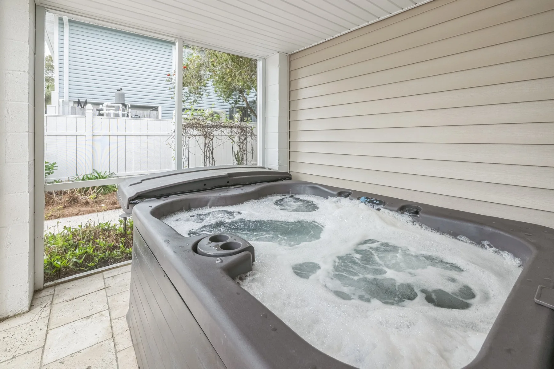 A bubbling hot tub sits beside large windows in a covered patio area.