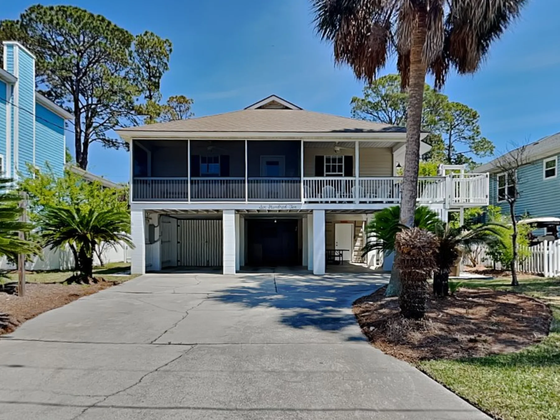 A raised house with a long balcony overlooks a wide concrete driveway.