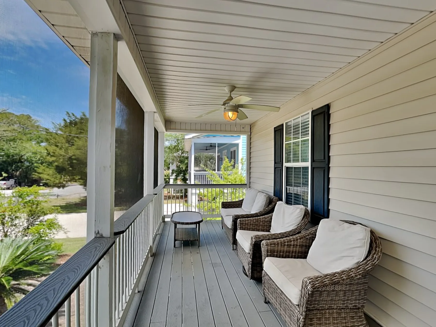 A covered porch with wicker seating and a ceiling fan.