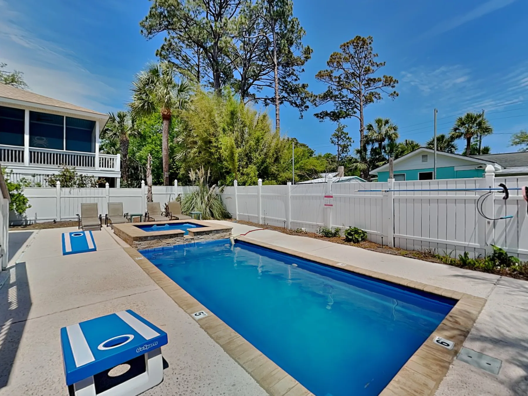 An outdoor swimming pool beside a paved deck and white fence.