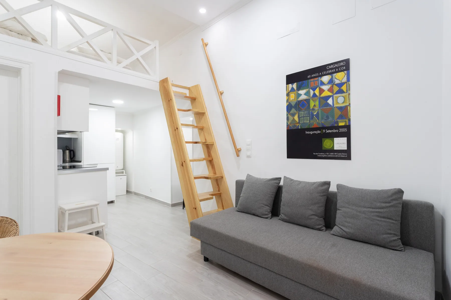 Una sala luminosa con asientos grises, una escalera de madera y una cocina abierta.