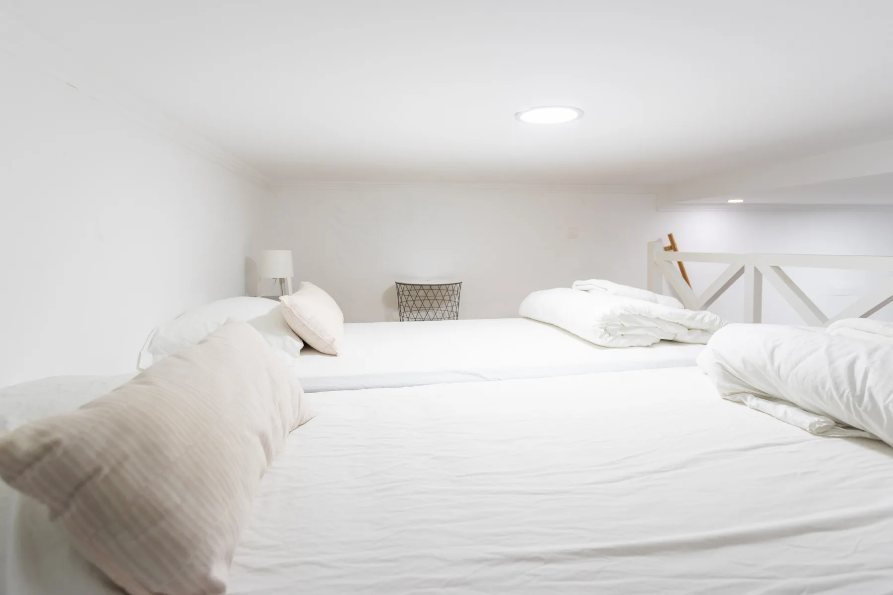 Una zona para dormir luminosa con ropa de cama blanca y una pequeña lámpara de noche.