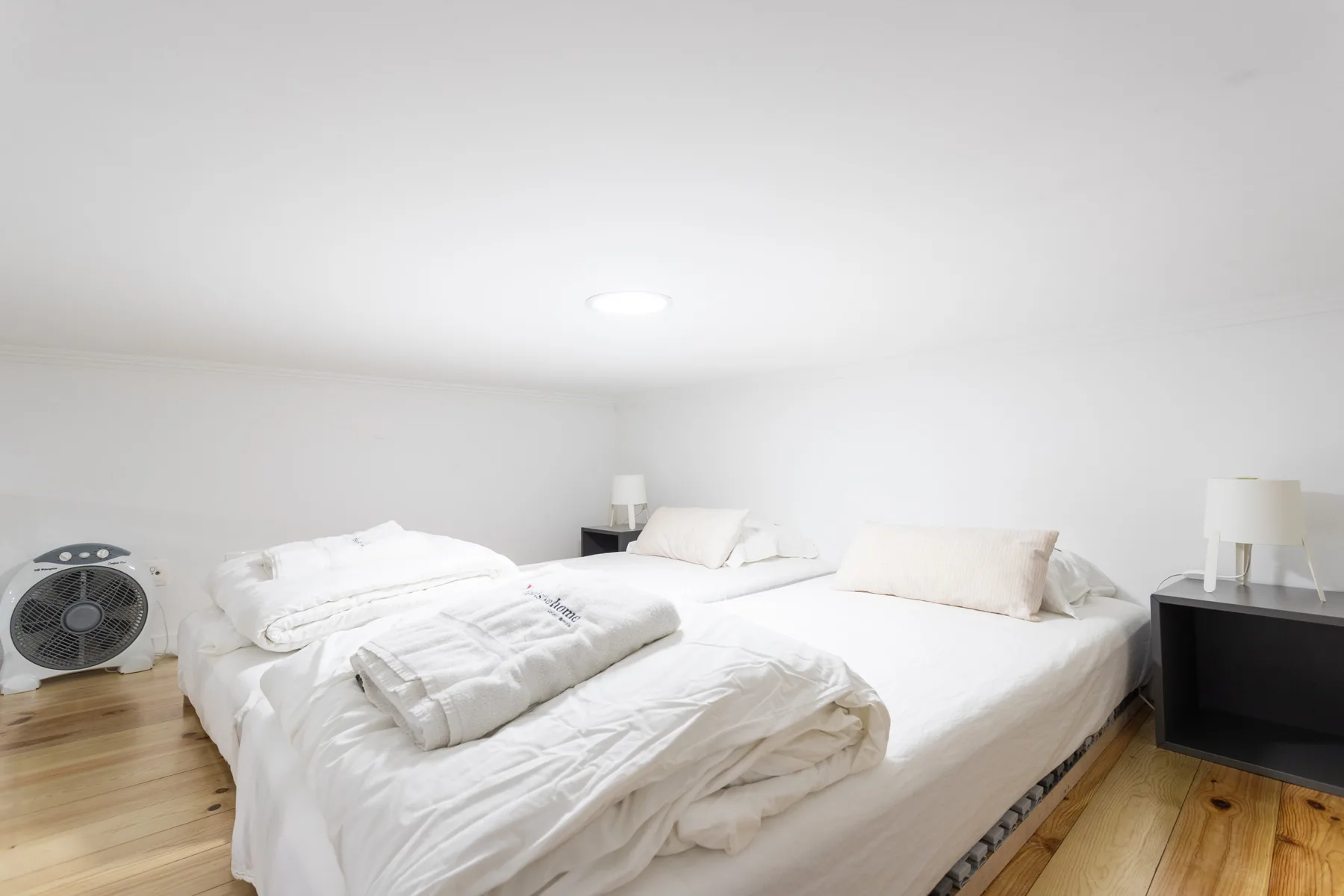 Dormitorio con ropa de cama blanca y suelo de madera clara.
