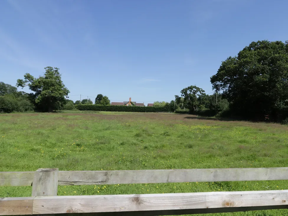 A green field with a wooden fence and trees in the background at The Bungalow in Dunnington