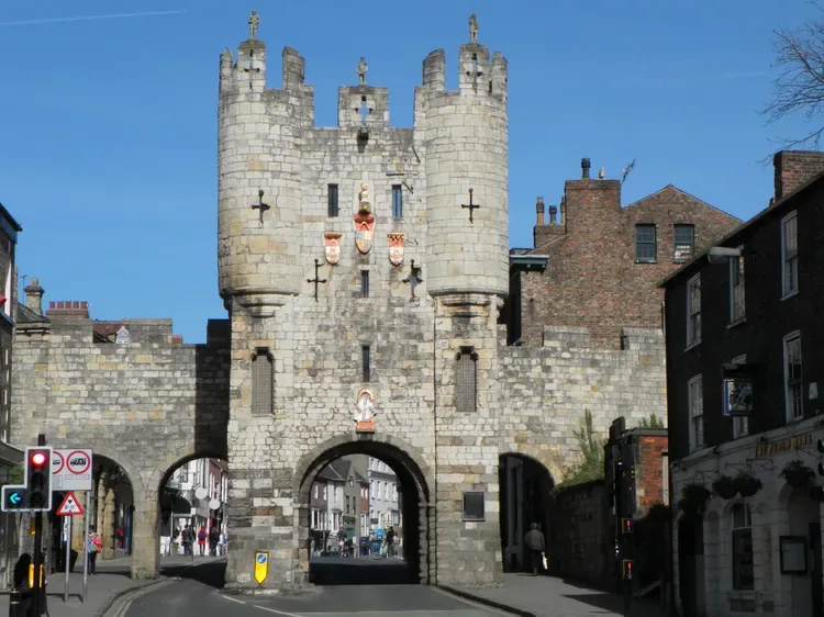 A stone gatehouse with a central arch stands between adjoining stone walls.