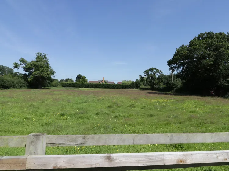 A grassy field stretches behind a low wooden fence beneath a clear sky.
