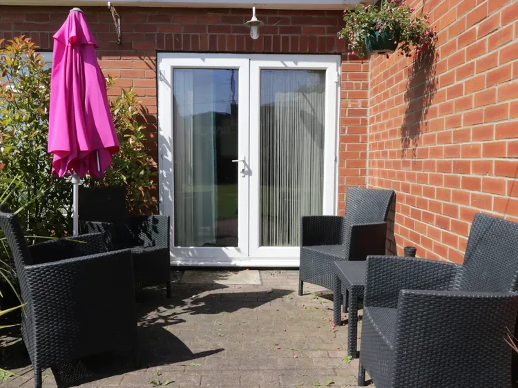 A brick patio with outdoor seating and a closed pink umbrella.