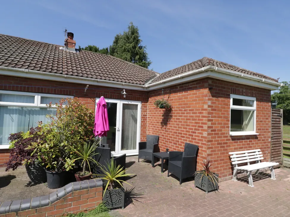 A brick house patio with dark outdoor seating, potted plants, and a closed pink umbrella.