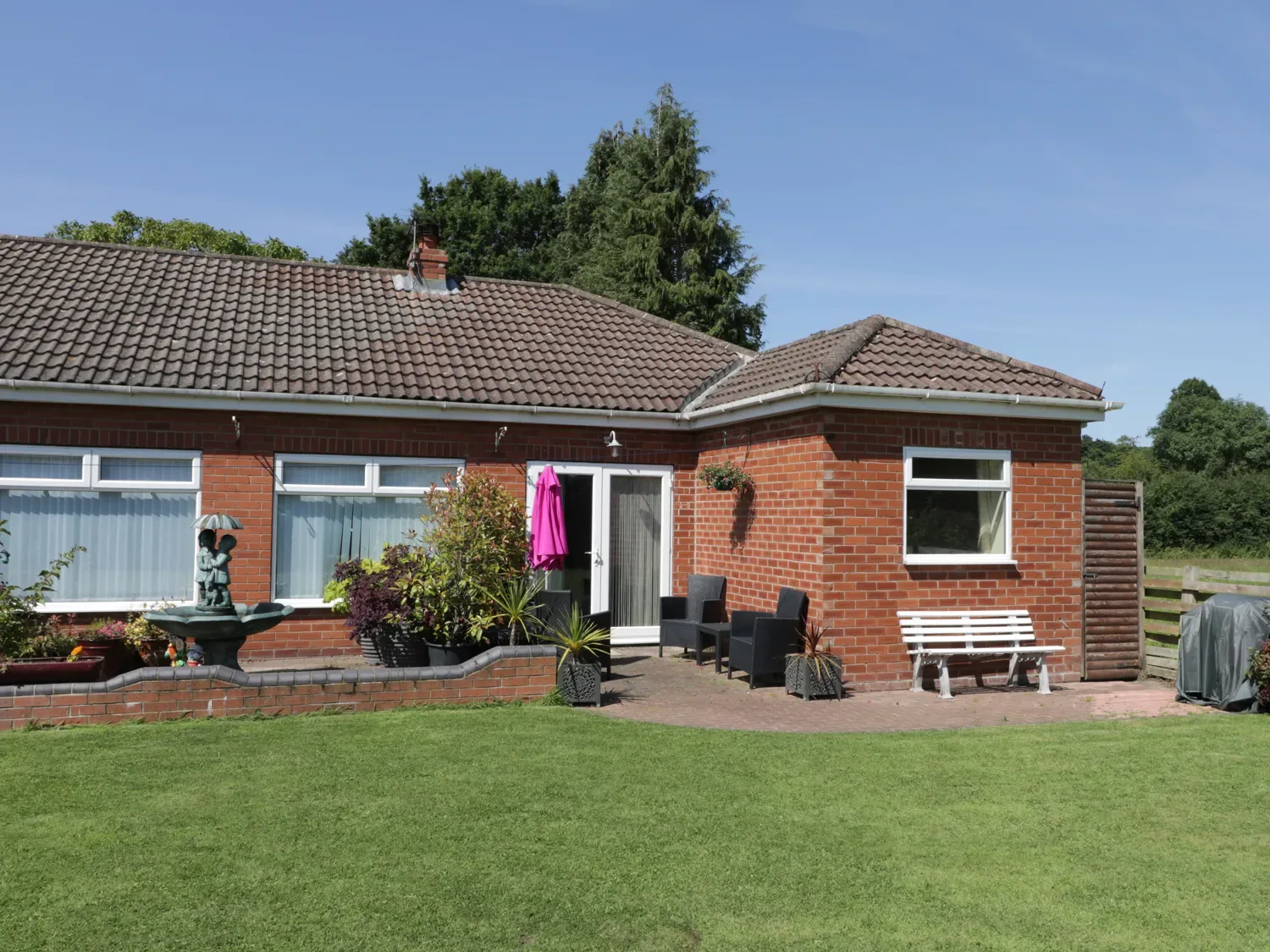 A brick bungalow with a tiled roof a lawn patio furniture and potted plants outdoors at The Bungalow in Dunnington