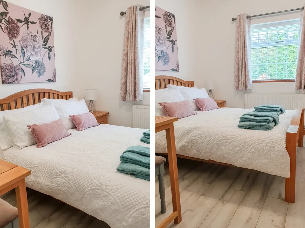A bedroom with a wooden bed, white bedding, pink cushions, and folded teal towels.