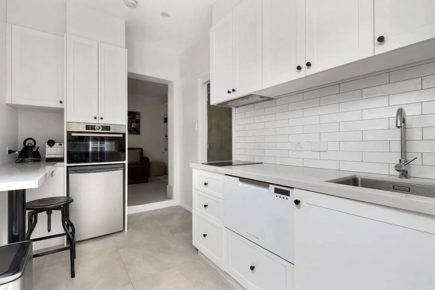 A bright white kitchen with built-in appliances and a long countertop.