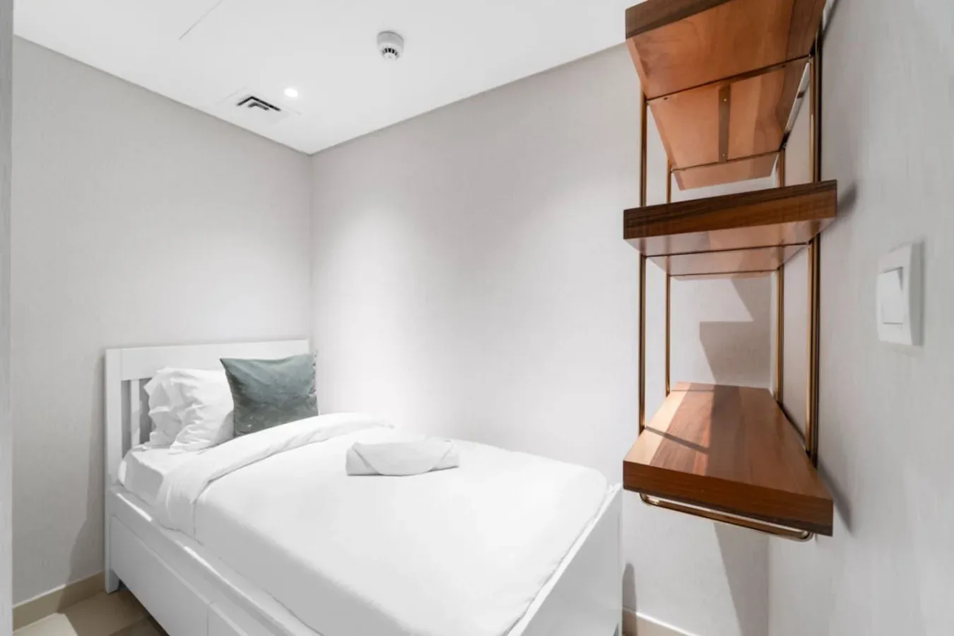A compact bedroom with a white bed and a wooden wall shelf.