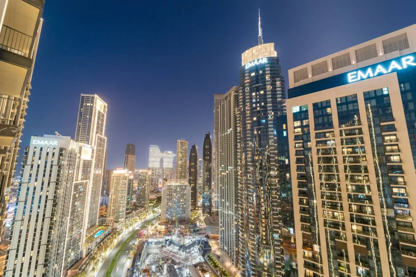 Nighttime city skyline with illuminated high-rise buildings and a busy roadway below.