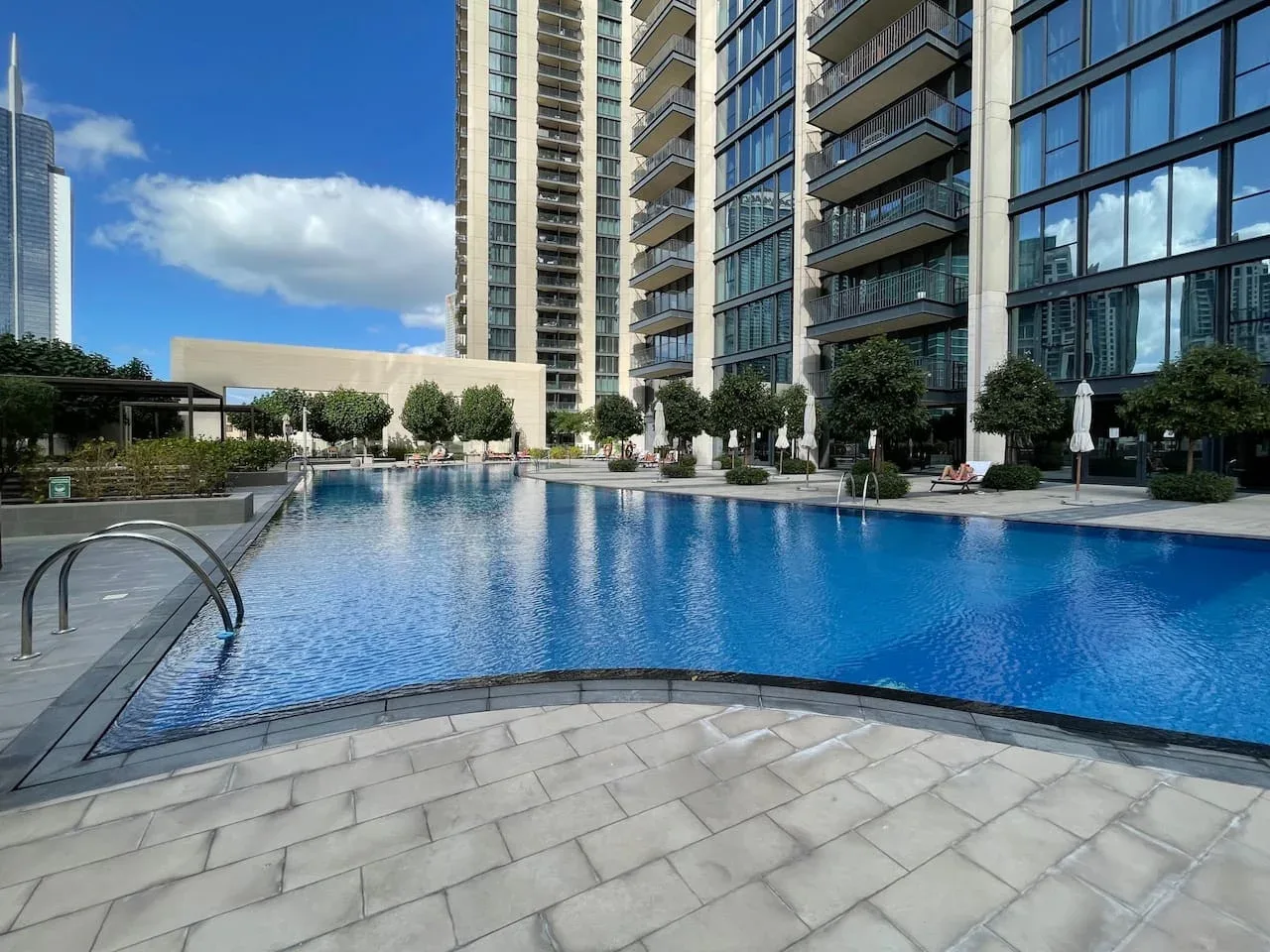 A swimming pool sits beside modern high-rise buildings and a paved deck.