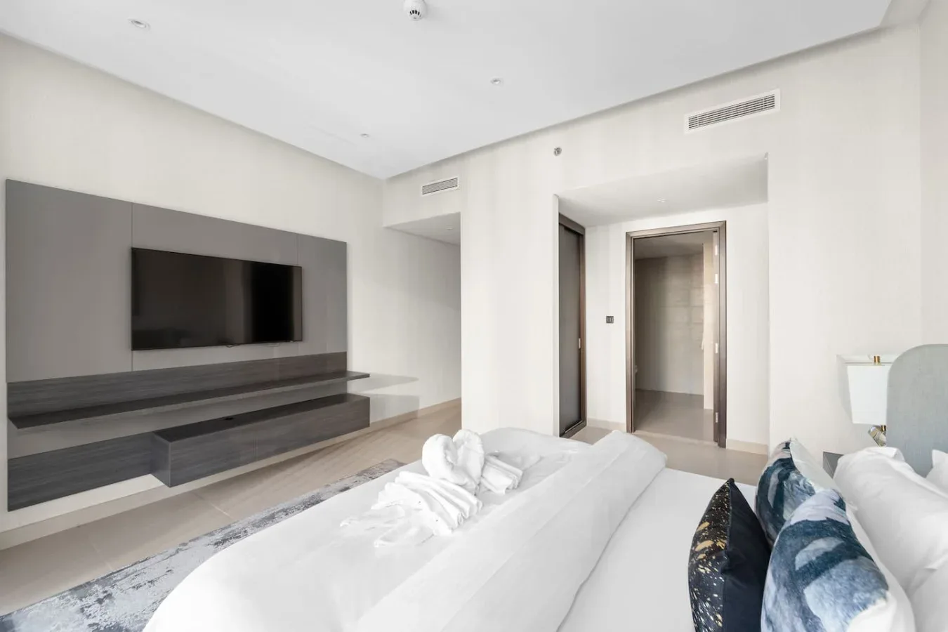 A bright bedroom with a large bed facing a wall-mounted television.