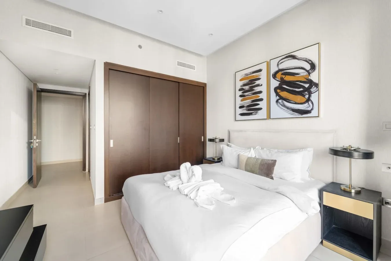 A bright bedroom with a neatly made bed and abstract artwork above it.