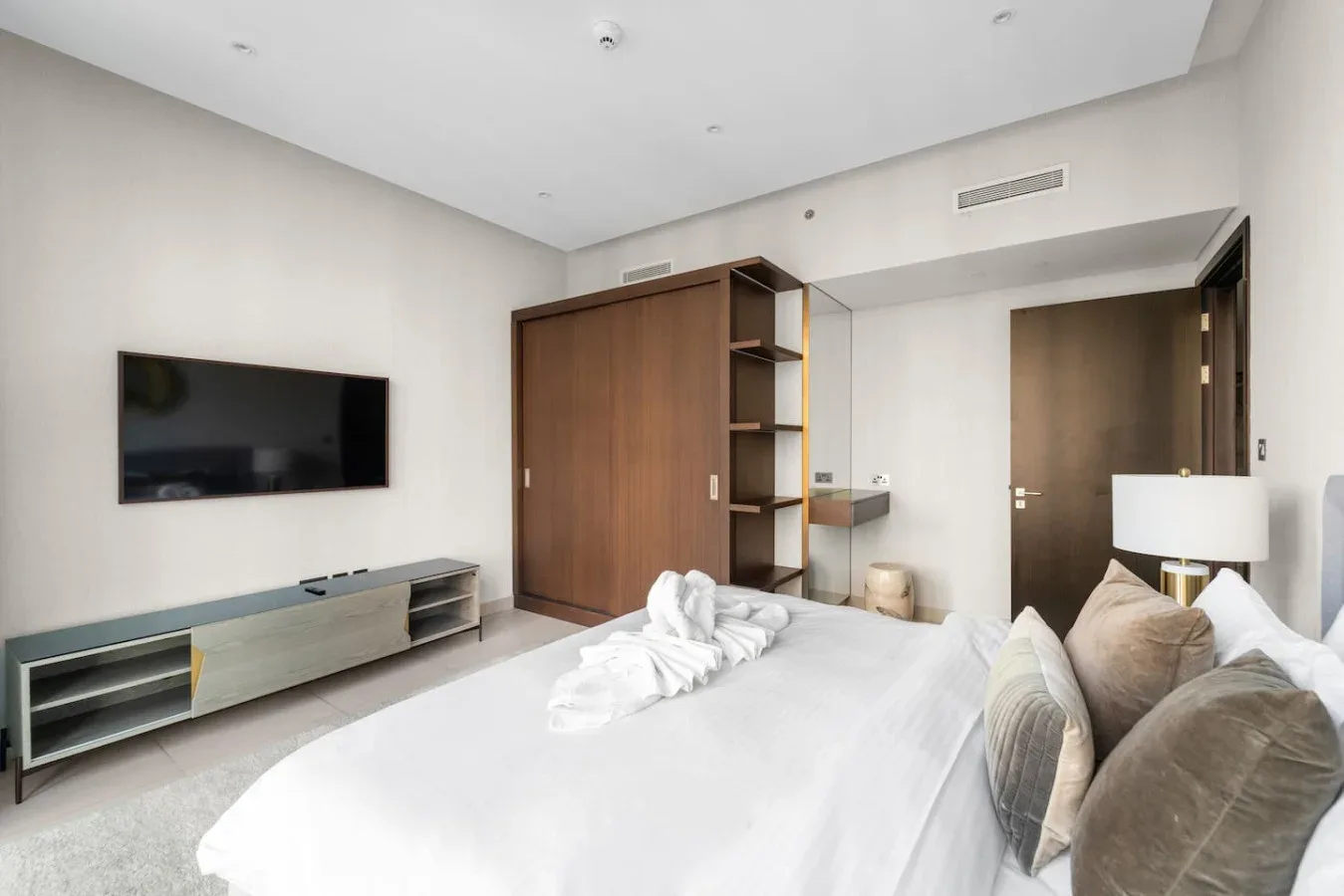 A bedroom with a large bed, wall-mounted television, and wooden wardrobe.