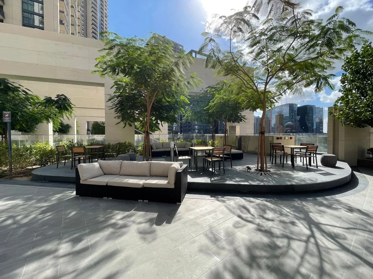 An outdoor terrace has seating and tables beneath leafy trees.