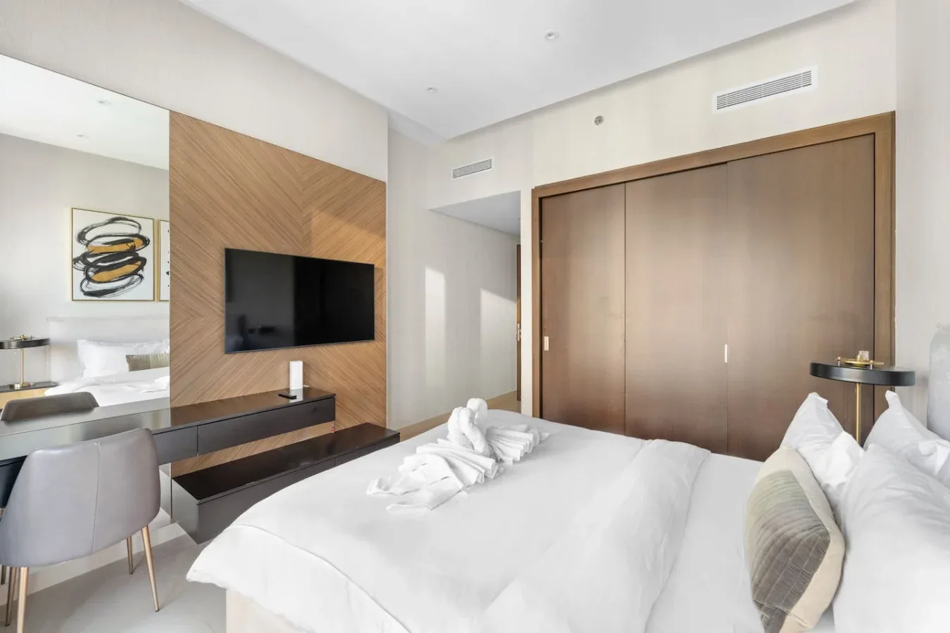 A bright bedroom with a large bed, wall-mounted television, and wooden closet doors.