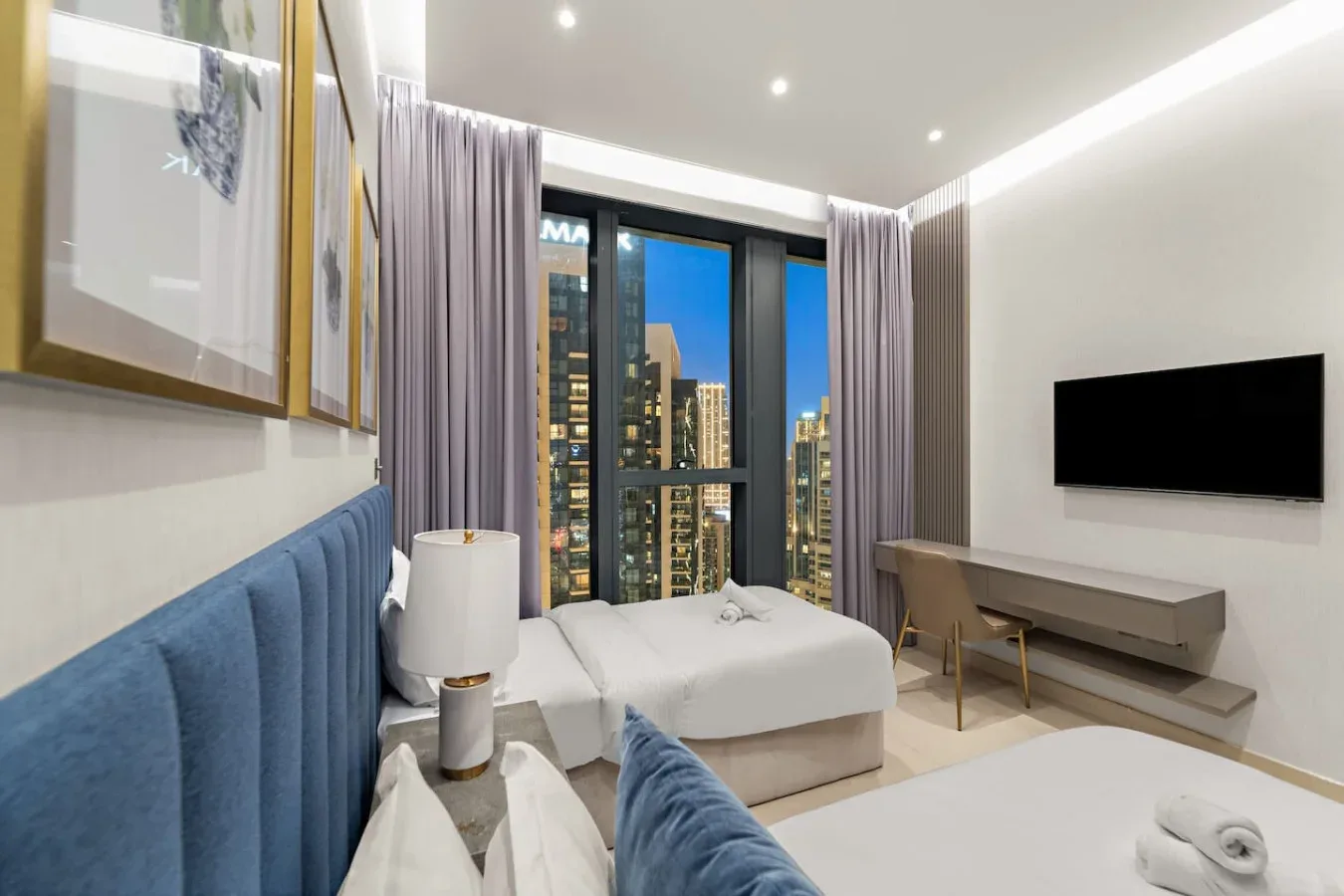 A bedroom with a bed, blue upholstered seating, and a wall-mounted television.
