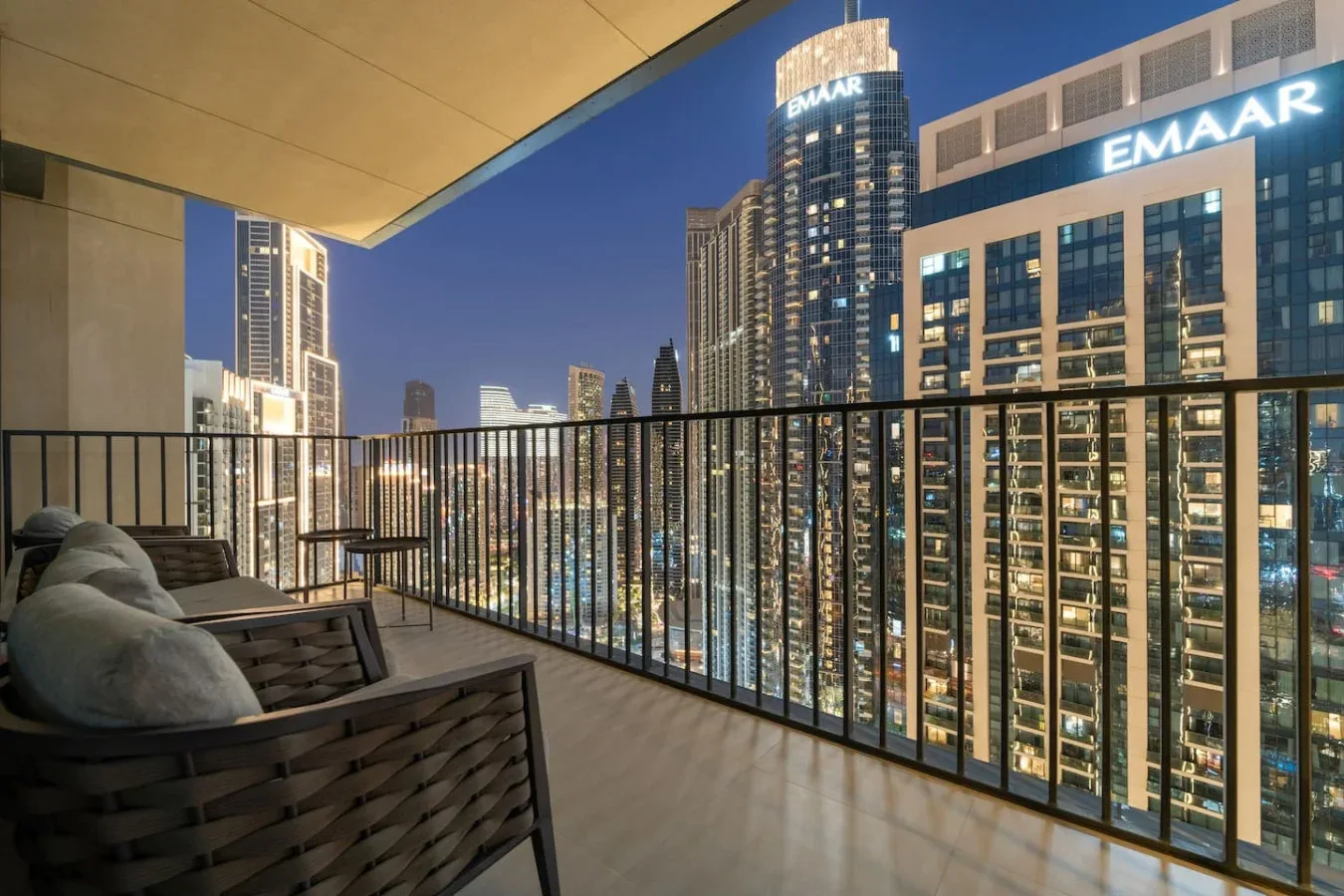 A balcony seating area overlooks illuminated high-rise buildings at night.