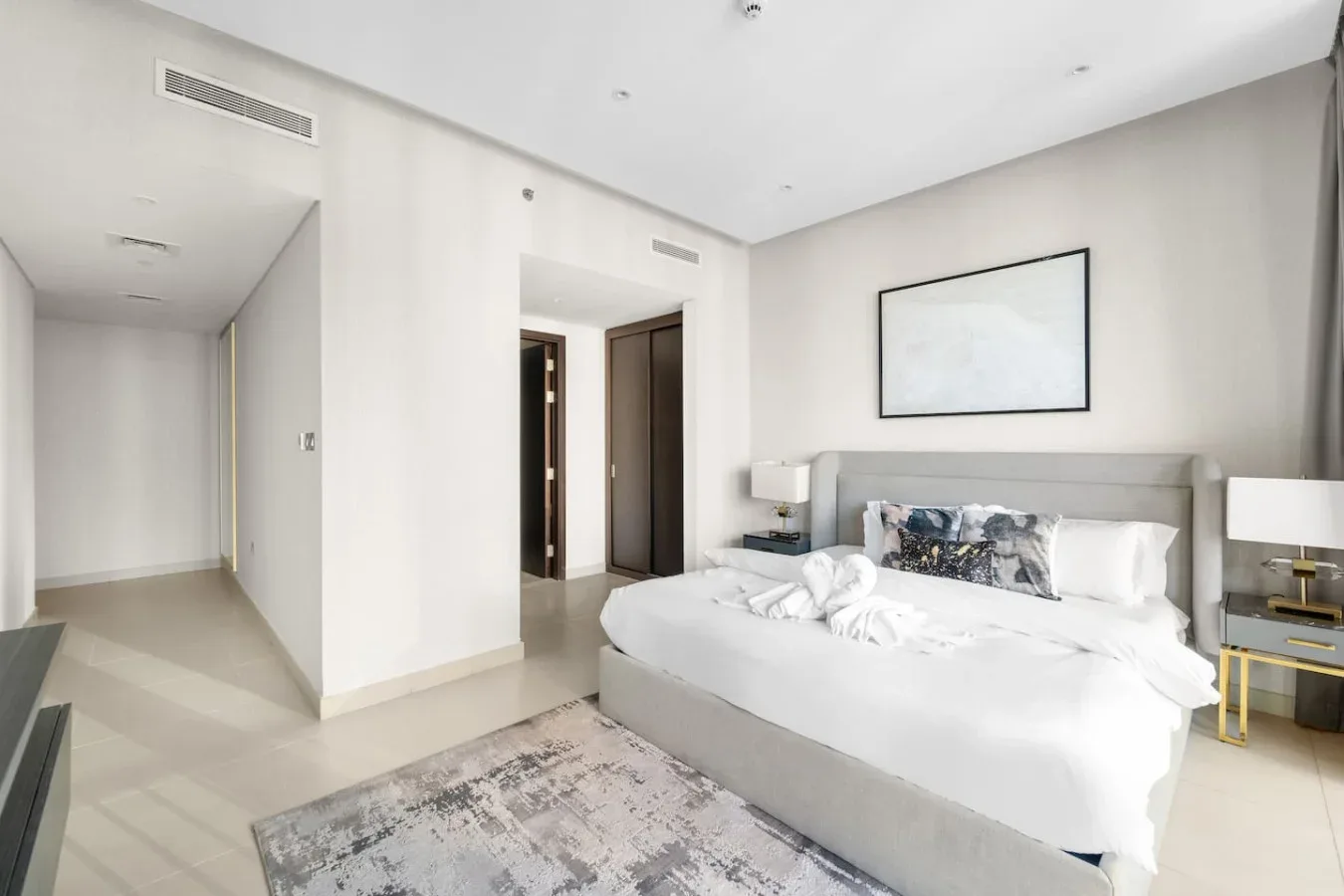 A bright bedroom with a large bed, bedside tables, and framed wall art.