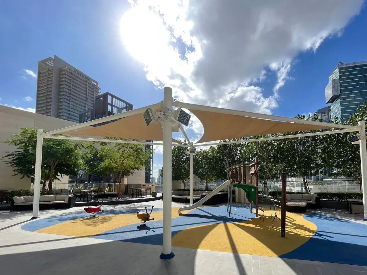An outdoor playground has colorful rubber flooring and shaded play equipment.