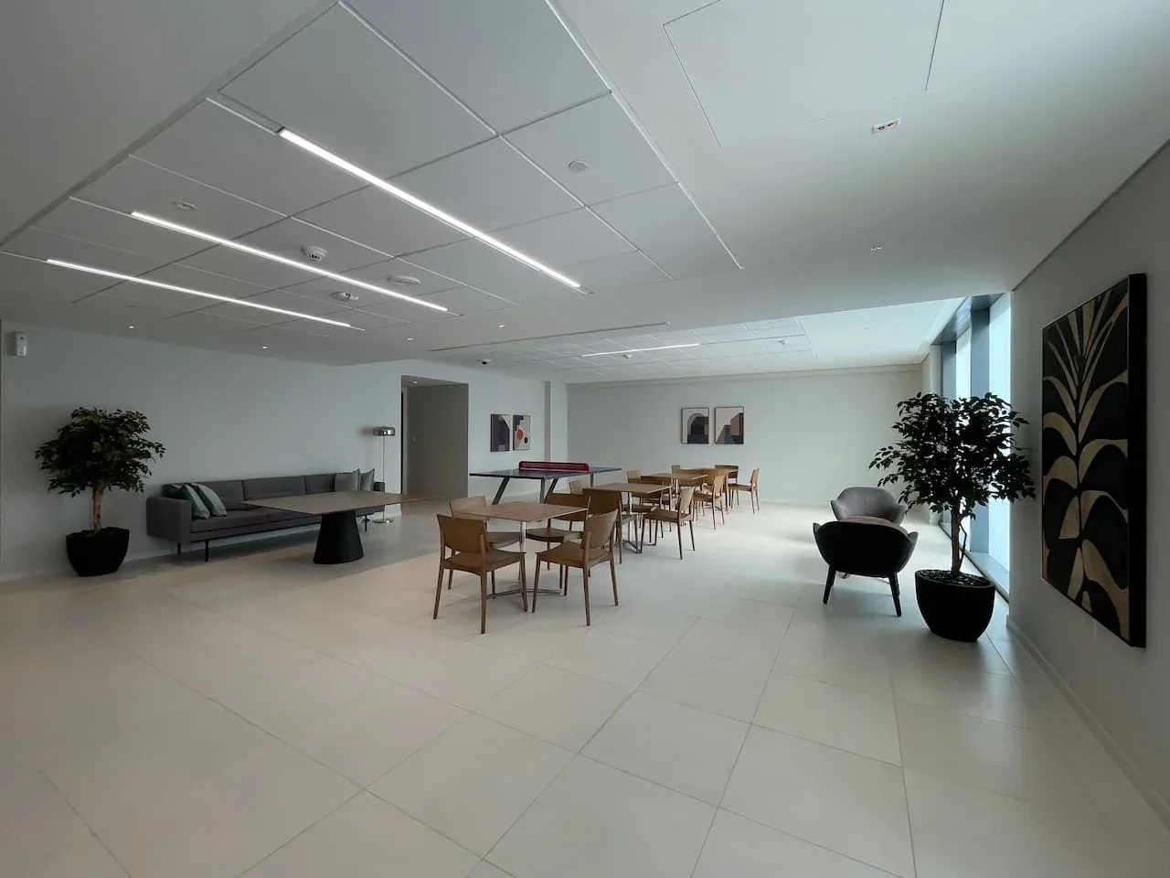 A spacious lounge with seating, tables, and potted plants.