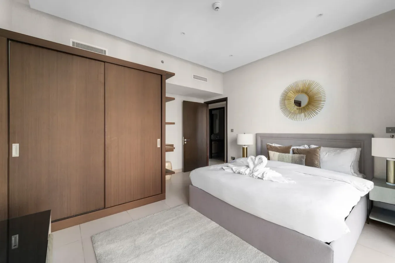 A bedroom with a neatly made bed, bedside tables, and a large wardrobe.