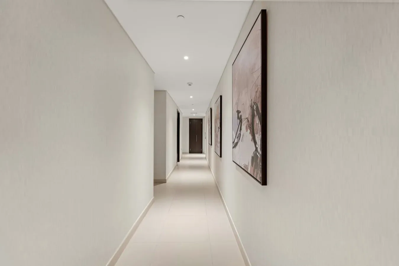 A bright hallway with light-colored walls, tiled flooring, and framed artwork.