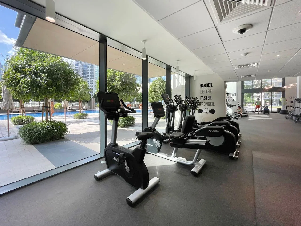 A gym with exercise bikes and other fitness equipment beside large windows.