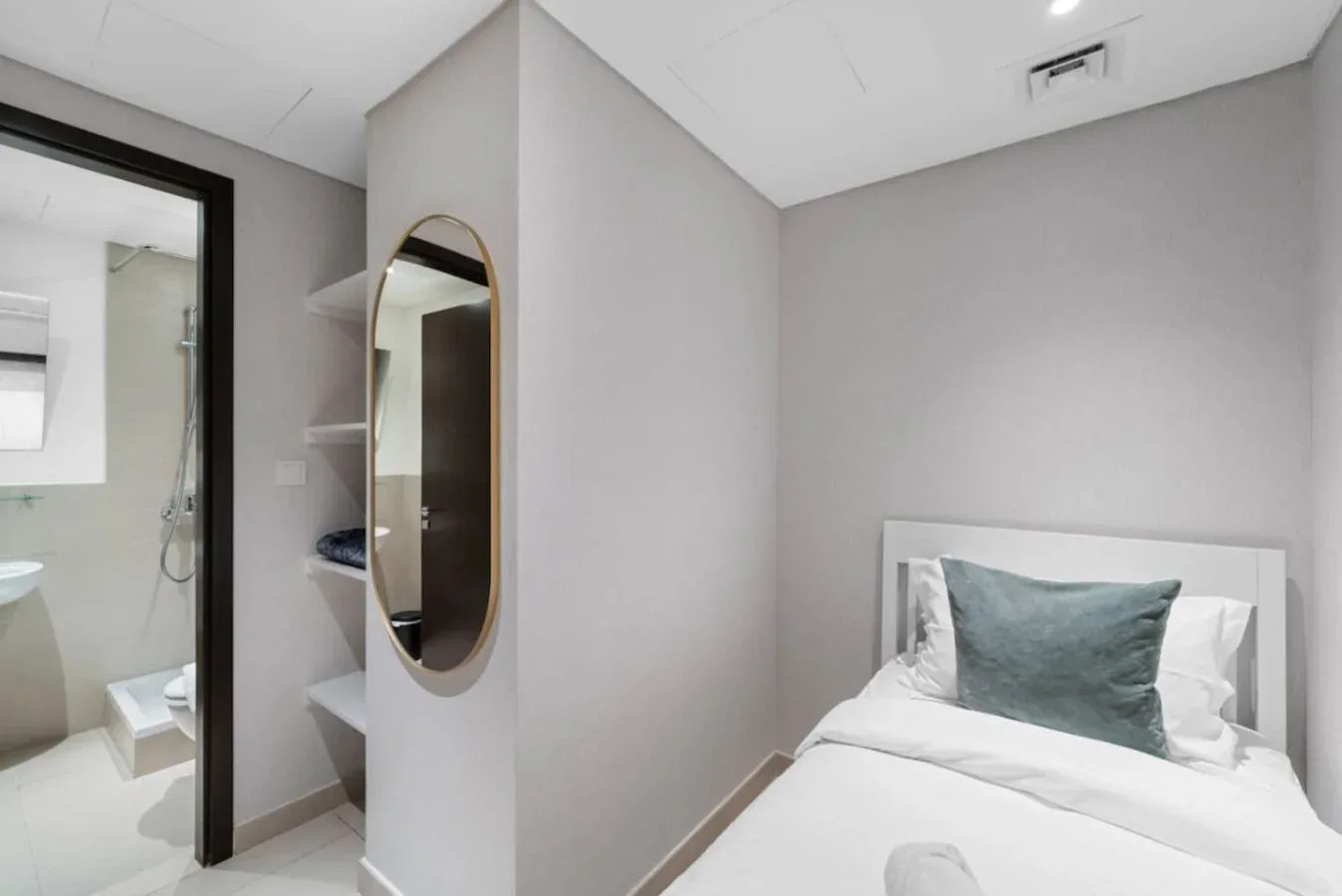 A bedroom with a neatly made bed and a bathroom visible through the doorway.