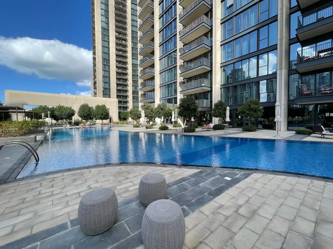 A swimming pool beside modern high-rise buildings, with paved seating areas.