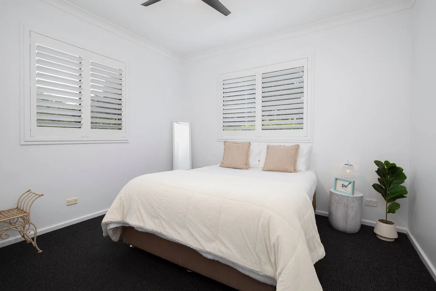A bright bedroom with a neatly made bed and shuttered windows.