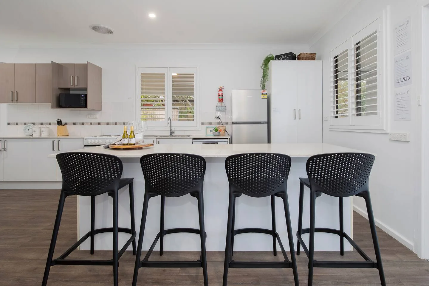 A bright kitchen has a long island with black seating and cabinets along the back wall.