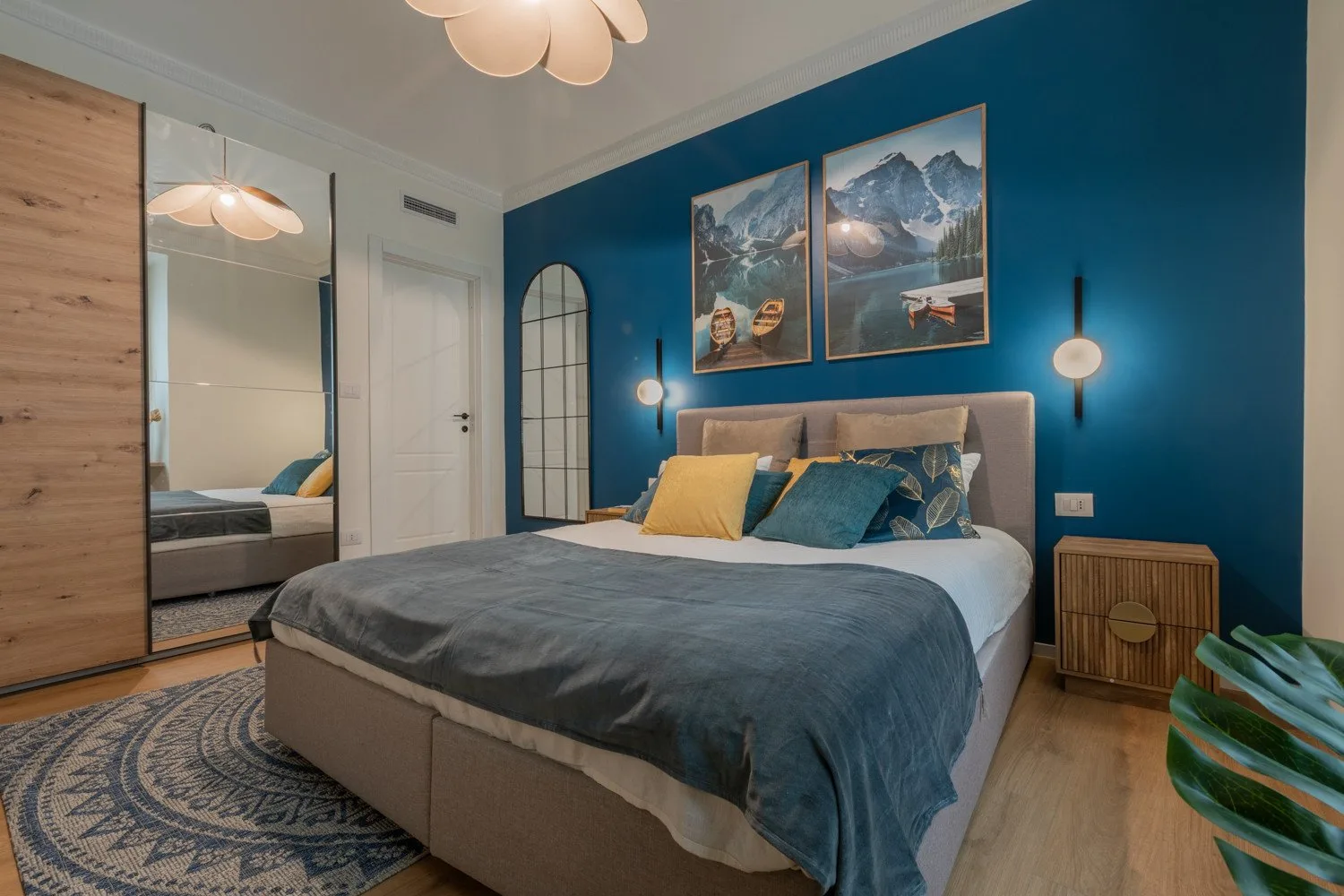 A bedroom with a bed against a teal wall and framed mountain artwork.