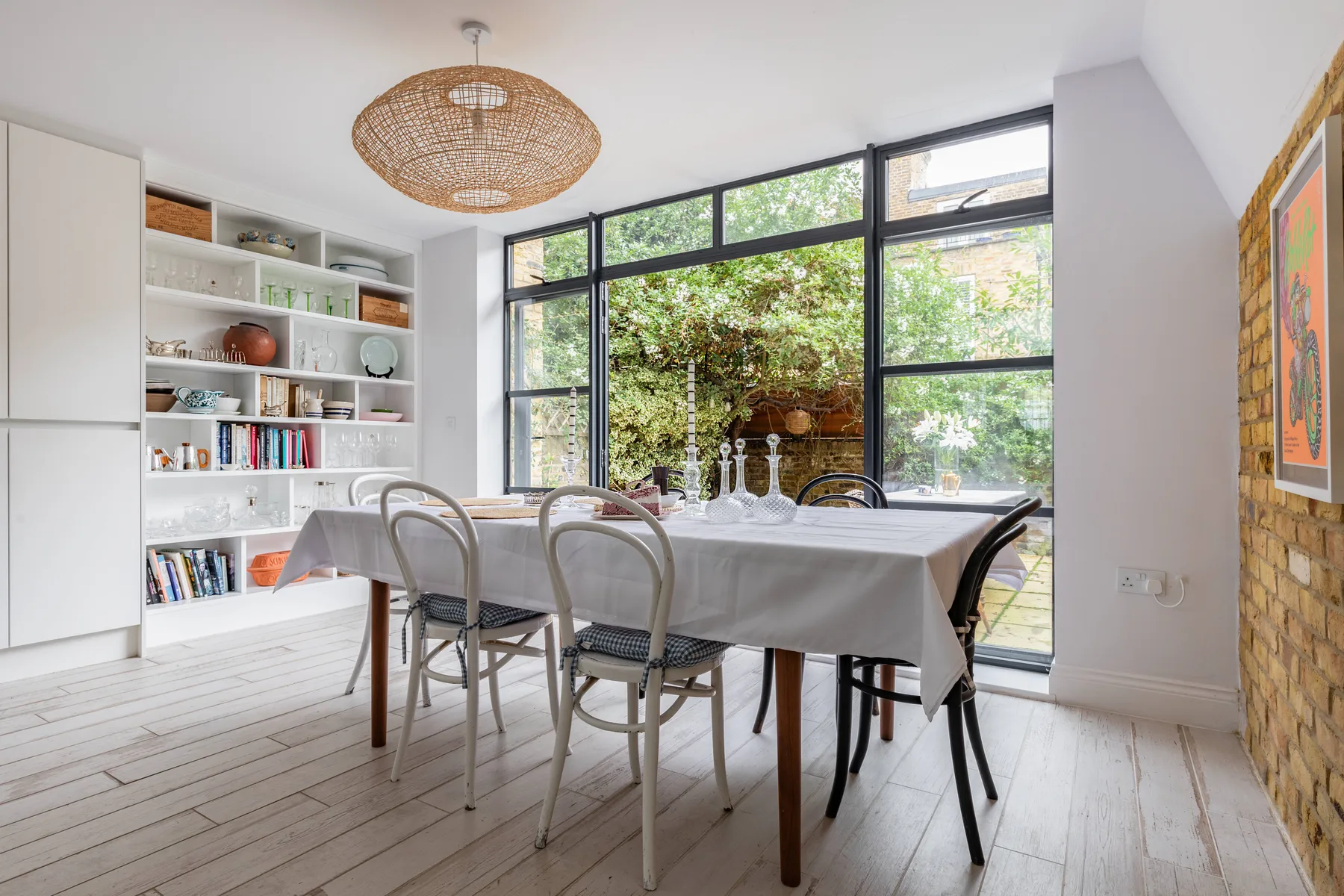Un comedor luminoso con la mesa puesta junto a grandes ventanas y estantes empotrados.