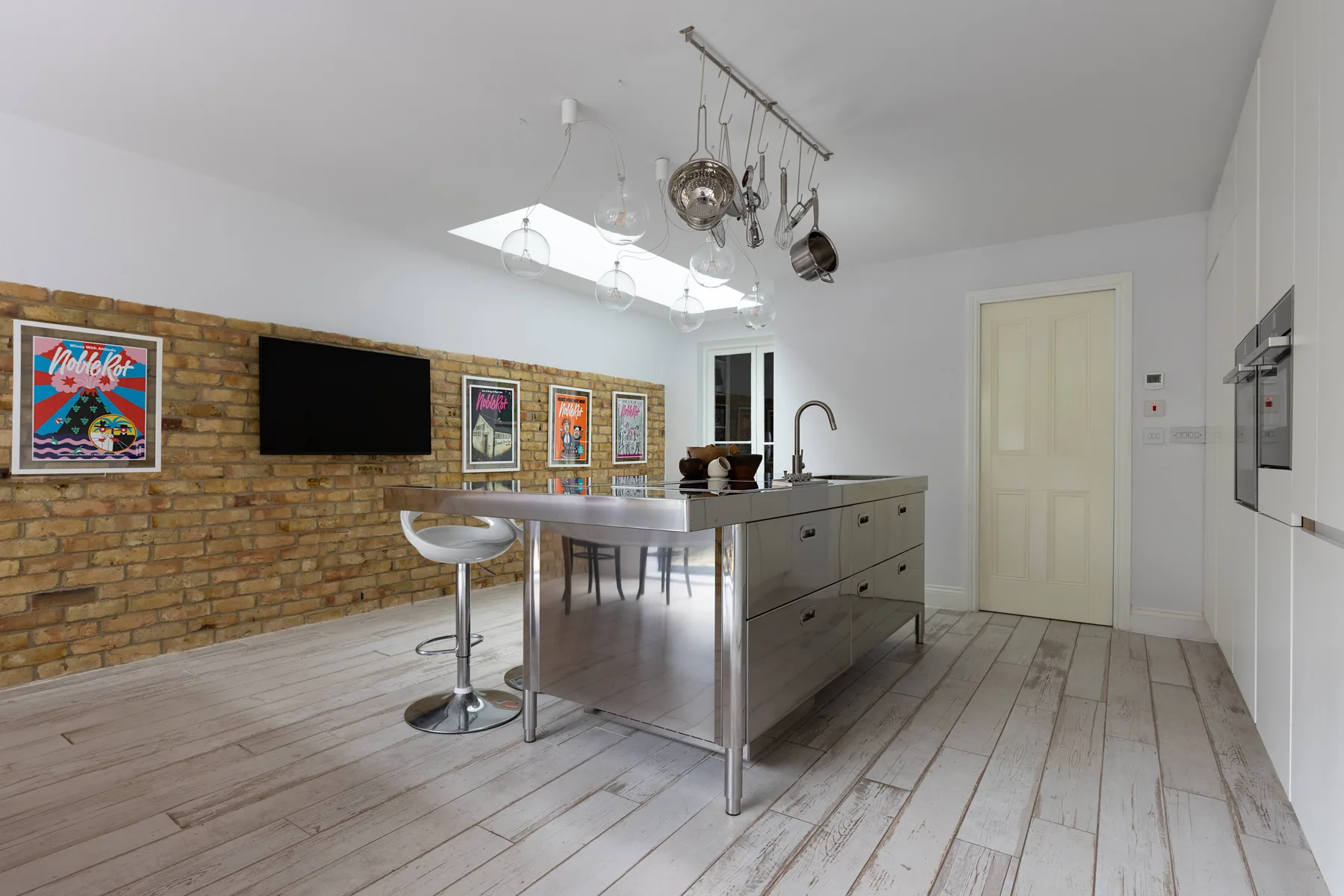 Una cocina luminosa con una isla central, utensilios colgantes y cuadros coloridos sobre una pared de ladrillo.