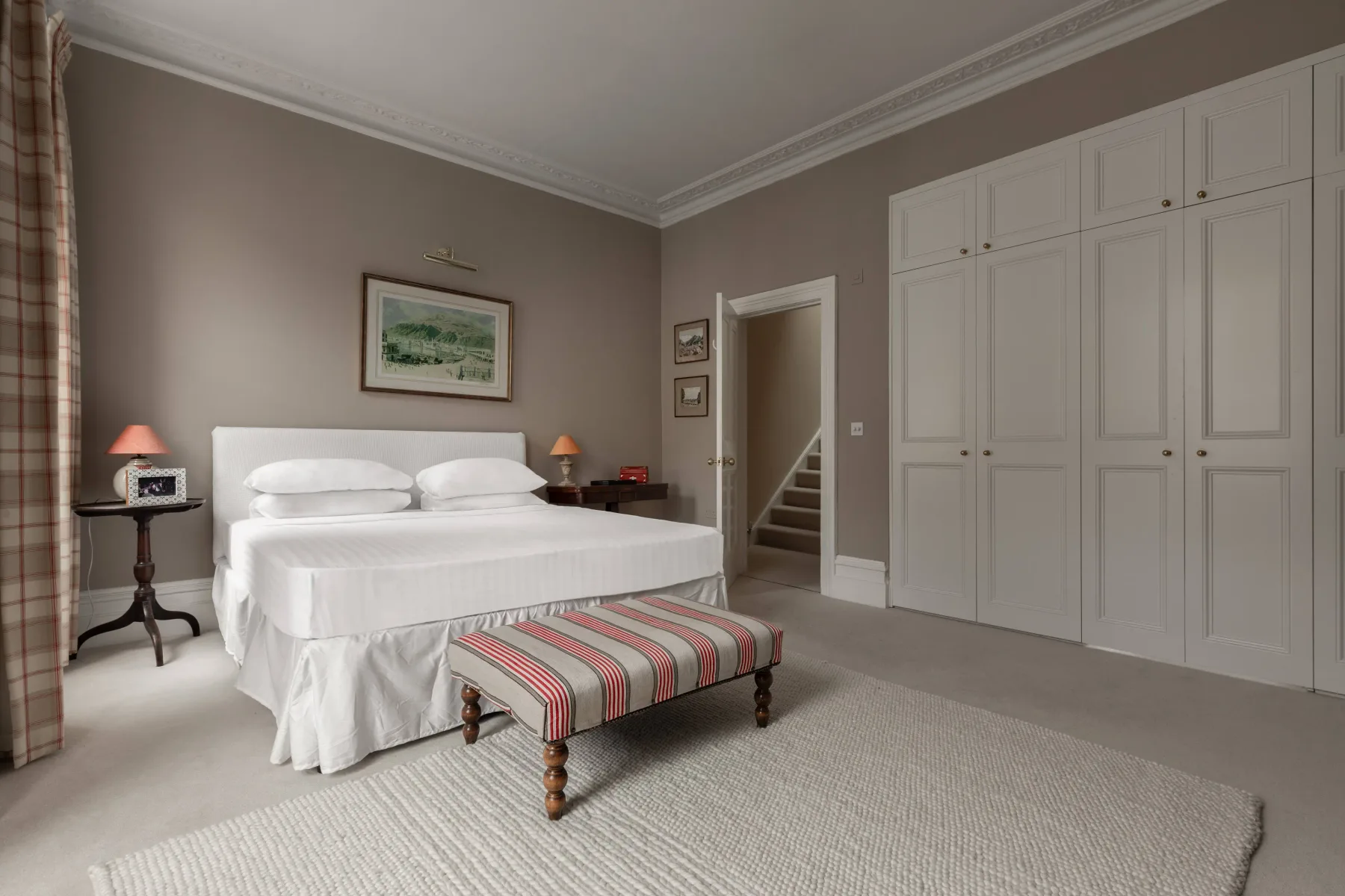 Un dormitorio con una cama bien tendida y un banco a rayas.